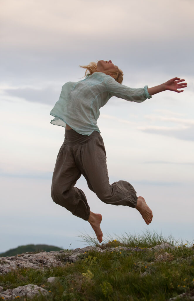 beautiful blonde girl dancer jumping over alpine meadow revealing bodies to the wind